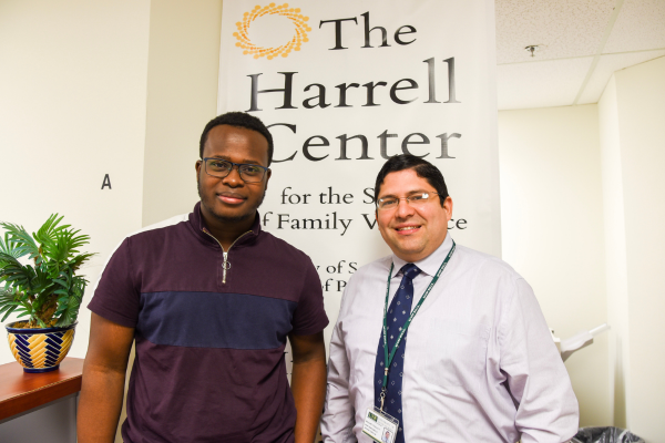 Dr. Salinas and a faculty member stand in front of a banner displaying "The Harrell Center," smiling.