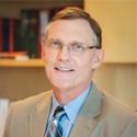 Dr. Stephen Liggett smiling wearing a blue dress shirt and tie with a tan suit jacket