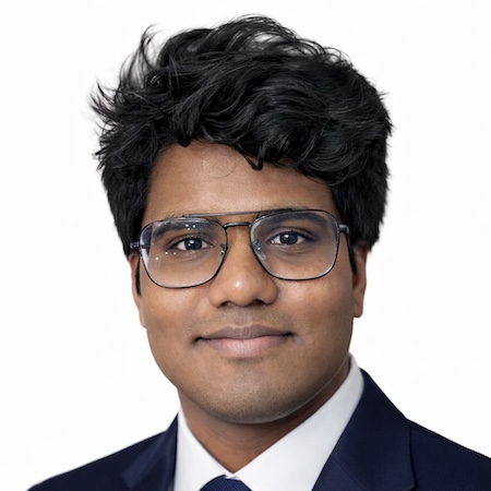 A man with dark brown hair smiles while wearing glasses and a suit