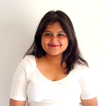 Female student with dark hair wearing a white shirt smiles for a picture