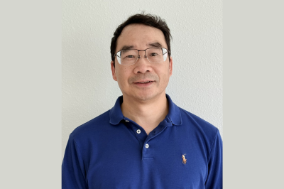 Dr. Song smiling wearing a blue polo shirt in front of a grey wall
