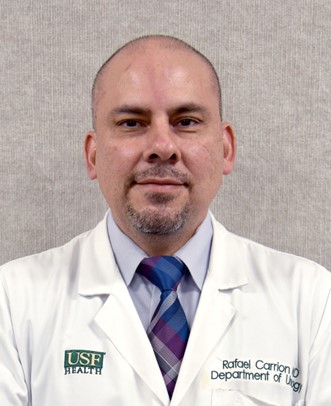 Dr. Carrion smiles wearing a USF Health medical white coat and multi-colored tie