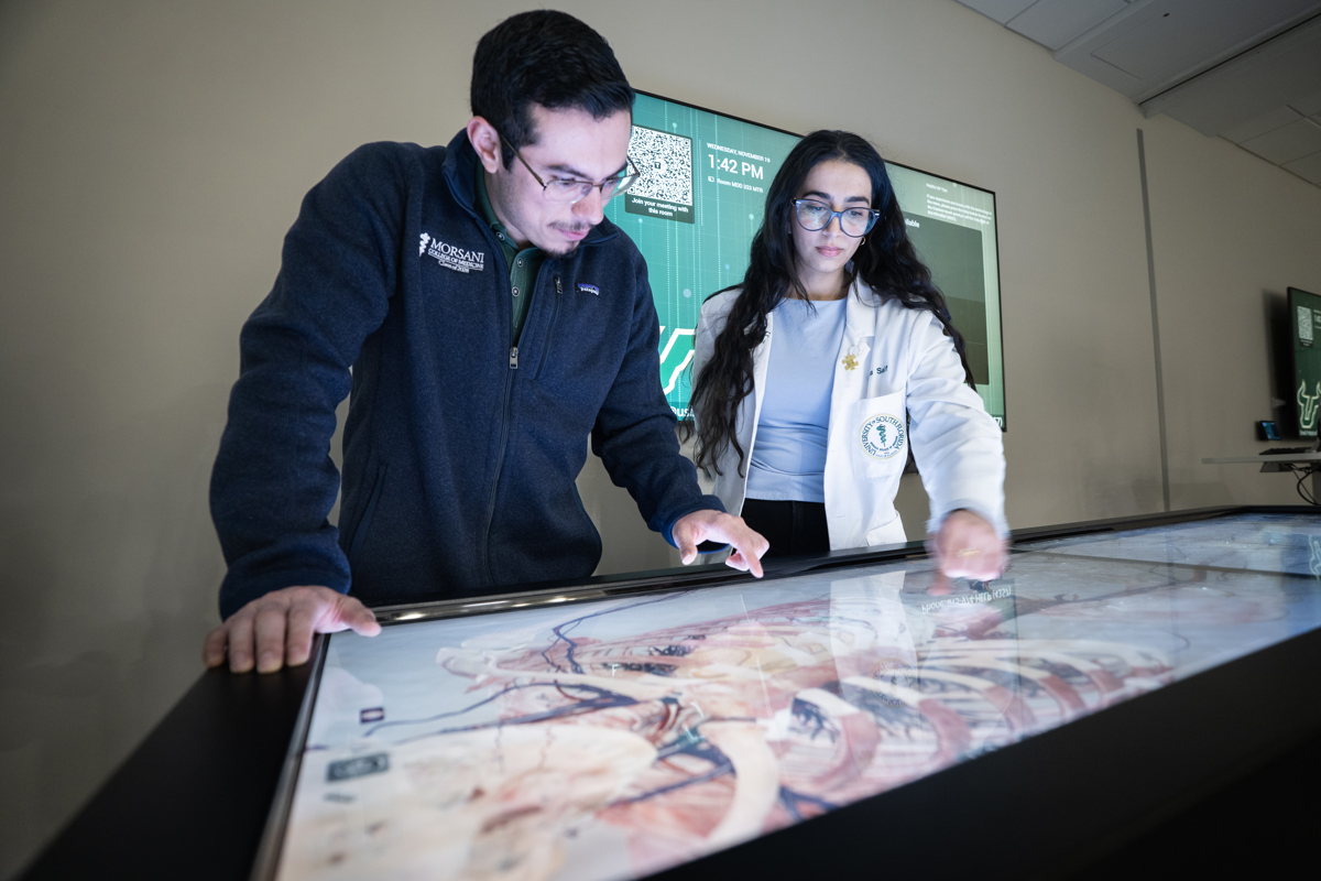 Two USF Health student looking down at a screen displaying an image of a human body