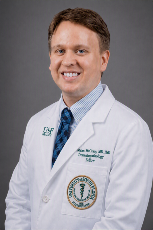 Dr. Myles McCrary smiling wearing a USF Health medical white coat, blue dress shirt and striped tie