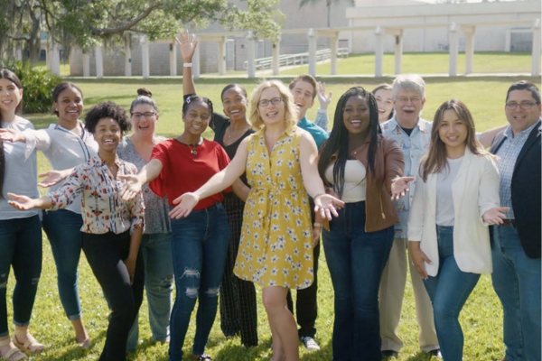 A group of individuals of various backgrounds stands in front of a building, showcasing camaraderie and community spirit.