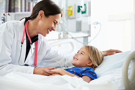 Dr. is attending to a smiling young girl in the hospital bed.